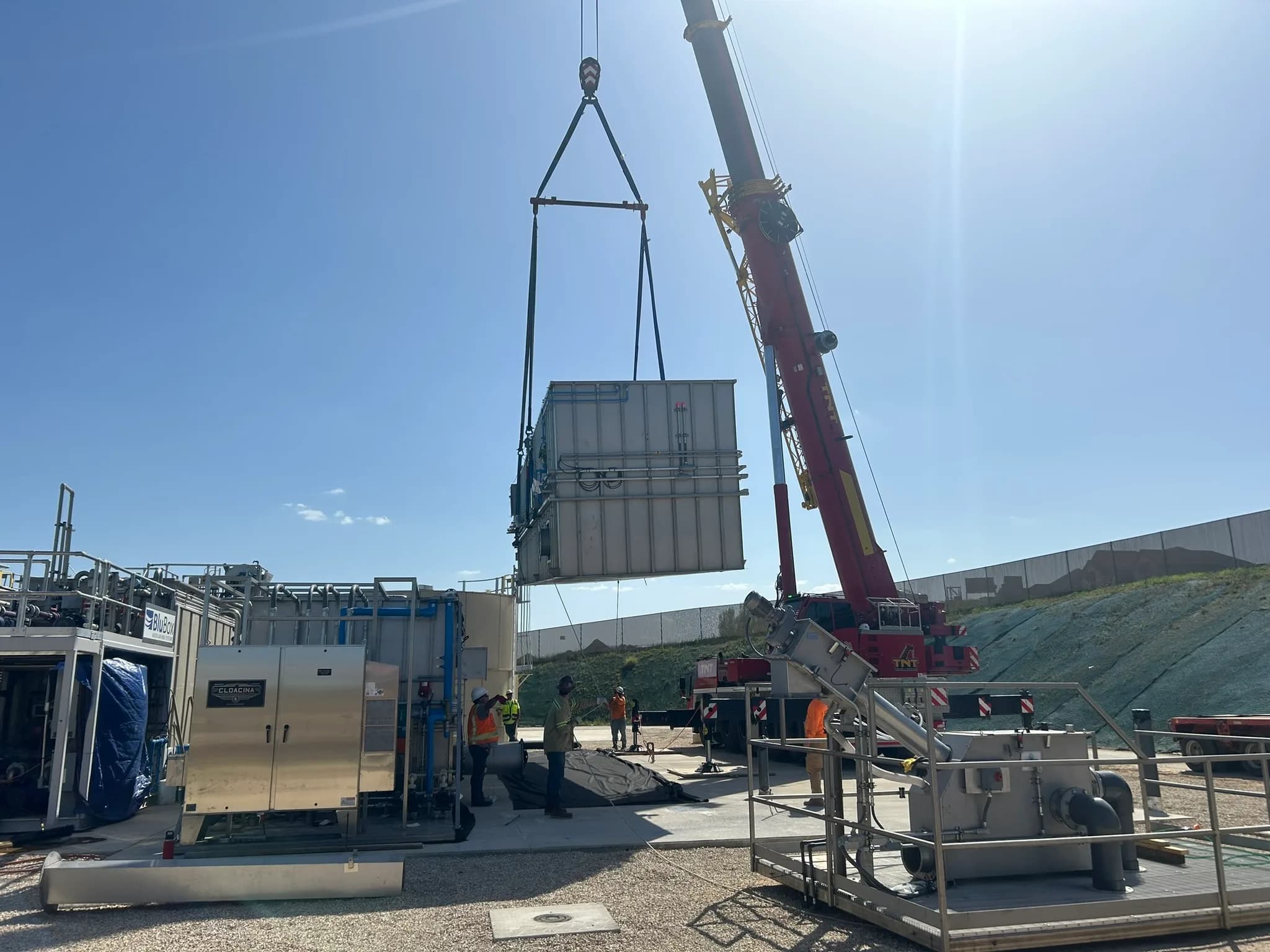 A crane lifts a packaged treatment module into place while crew members guide it.