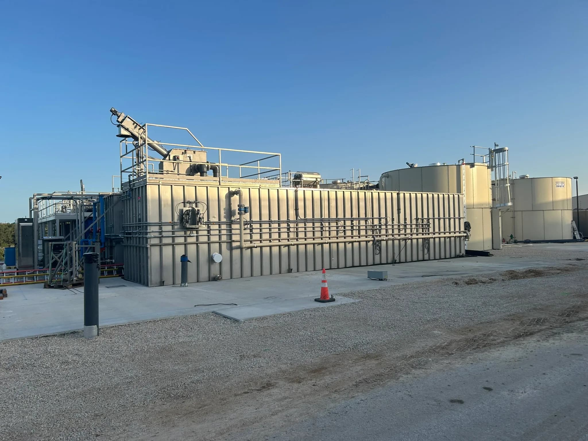 Packaged wastewater treatment plant with a long rectangular tank, an inclined screen and round tanks on a pad.