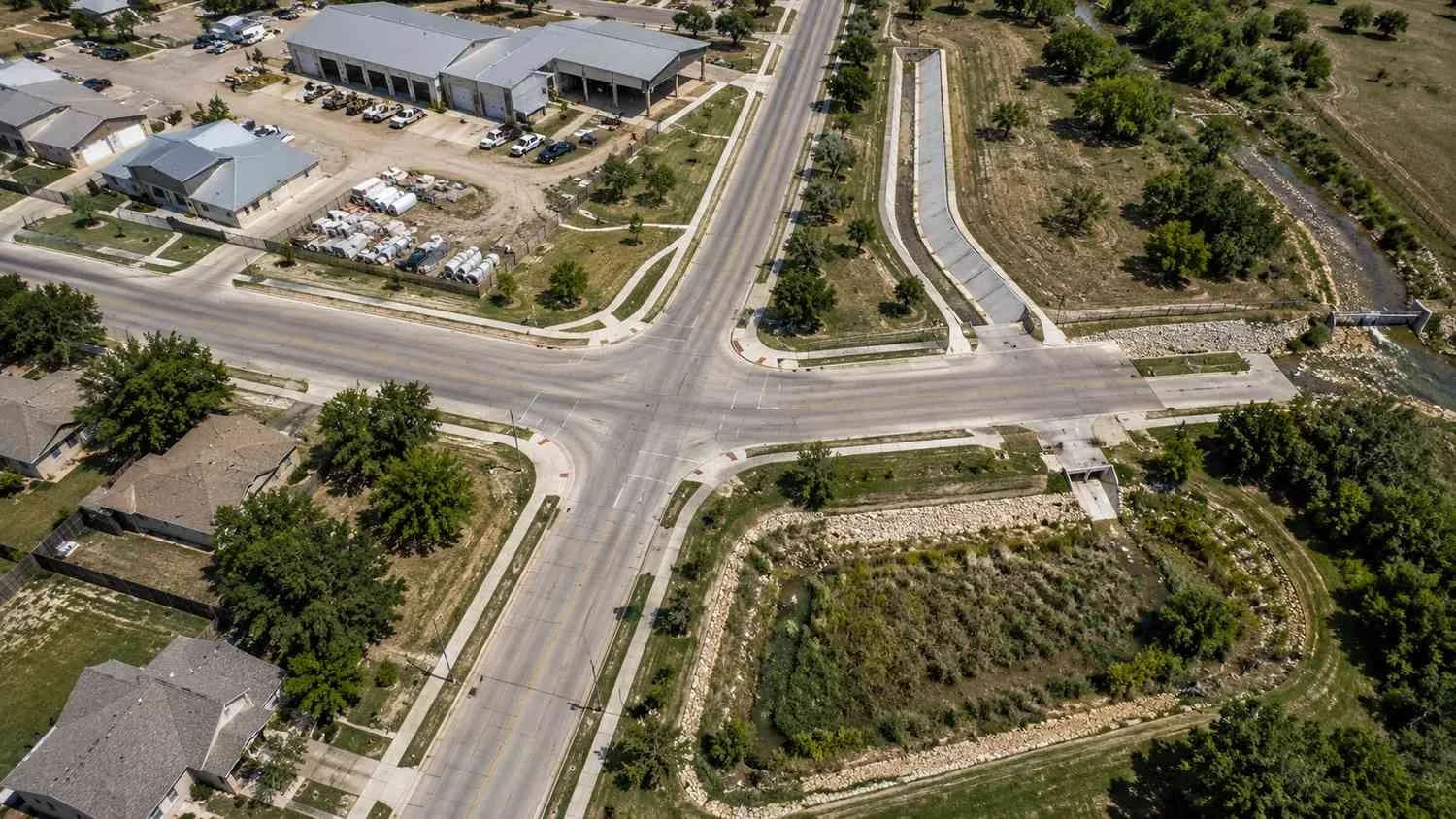 Top-down aerial view of a small Texas city showing storm sewer infrastructure including street drainage inlets, outfall structures discharging to a creek, and municipal facilities representing the regulated MS4 system requiring Phase II permit compliance