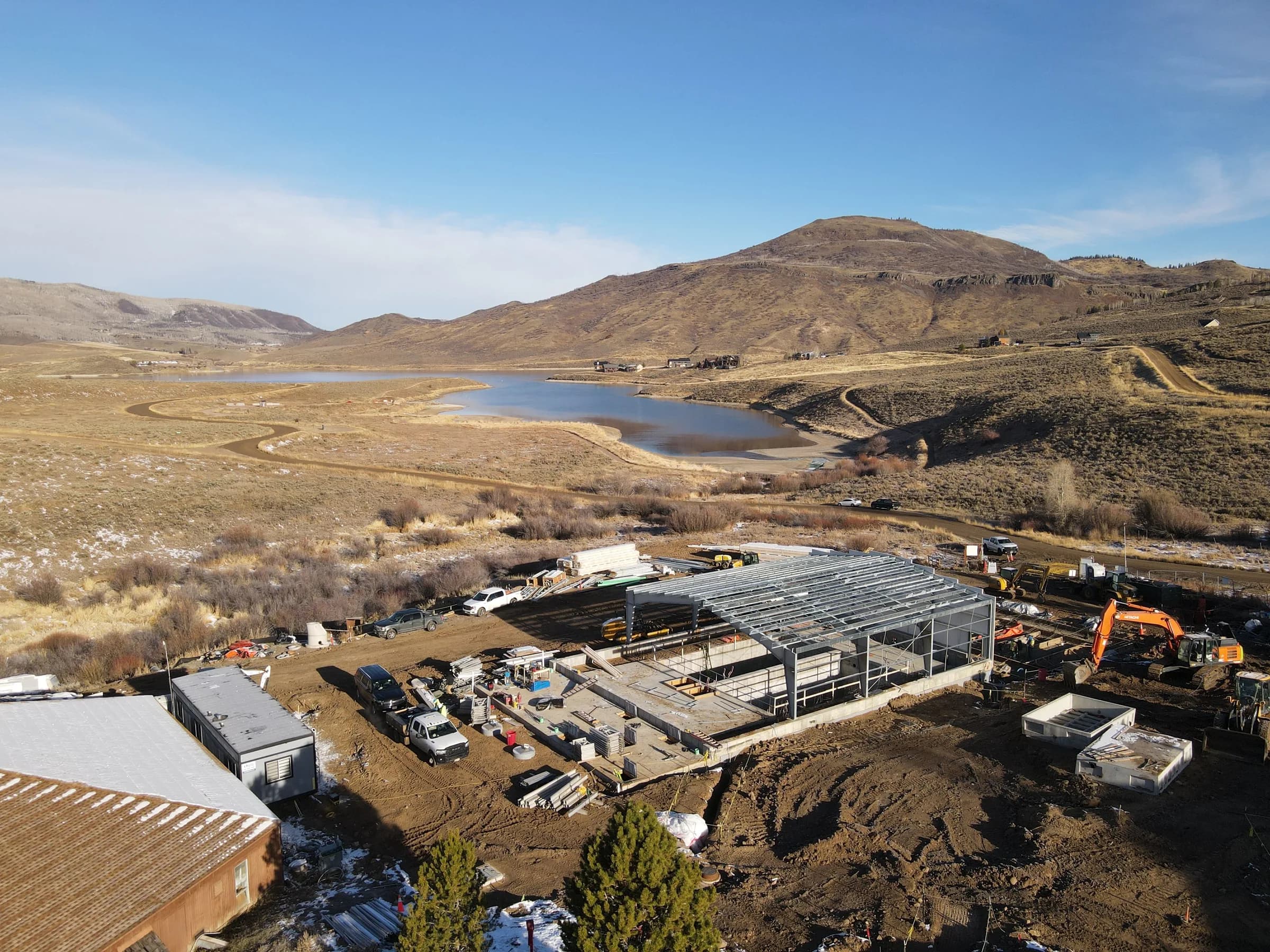 Aerial view of a wastewater treatment plant under construction in dry hills above a mountain reservoir.