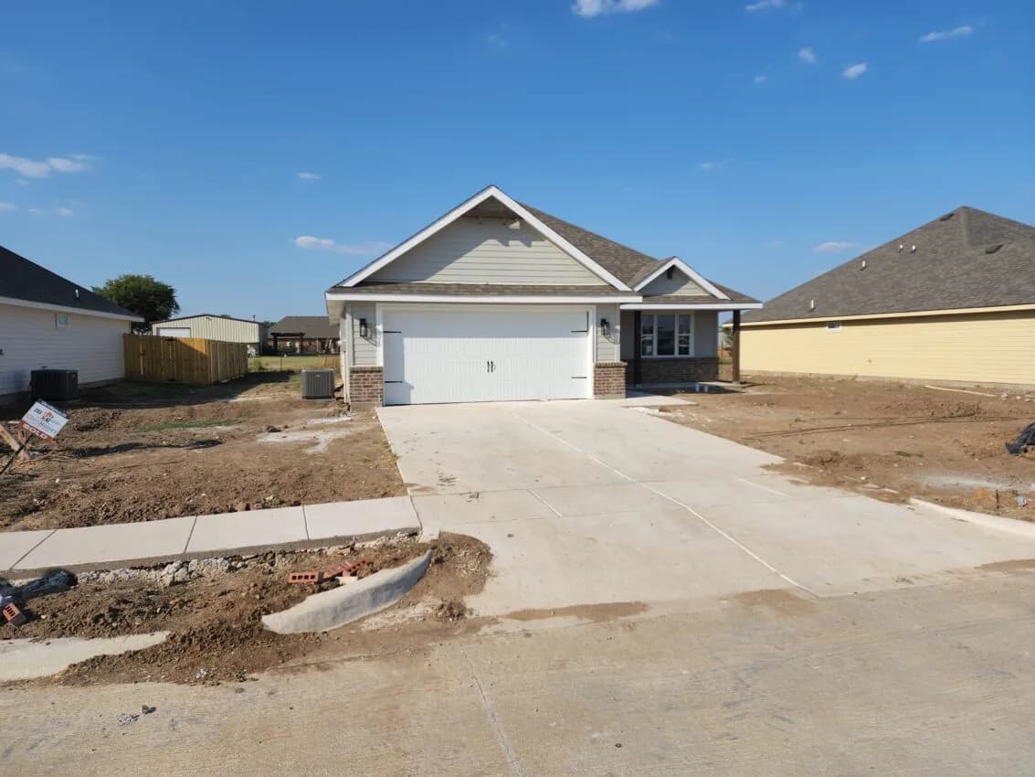 New single-family home with a concrete driveway and sidewalk, surrounded by bare graded lots in a new subdivision.