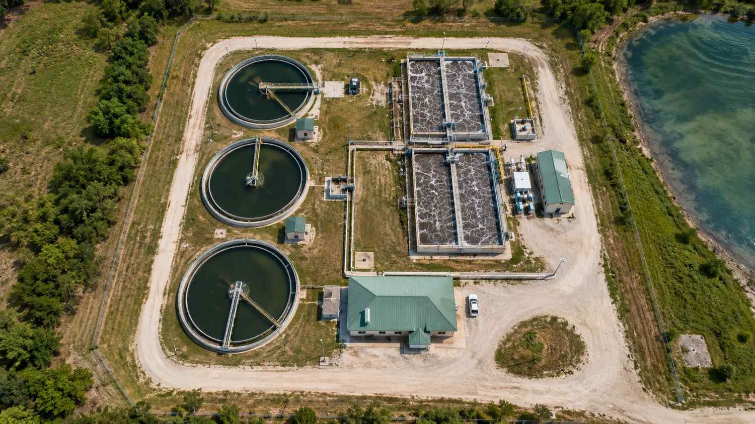 Top-down aerial view of a wastewater treatment plant showing multiple circular clarifier tanks, aeration basins, and treatment process infrastructure from above with engineering modeling equipment visible at an operations building