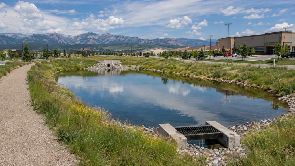 Aesthetically enhanced stormwater detention pond at a Colorado development site showing water quality features, native vegetation planting, riprap channels, and concrete outlet structure meeting Denver Wastewater Engineering Department design requirements