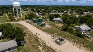 Top-down aerial view of a small Texas municipality showing aging water and wastewater infrastructure including a lift station, water tower, collection mains, and treatment facility representing the assets that belong in a capital improvement plan