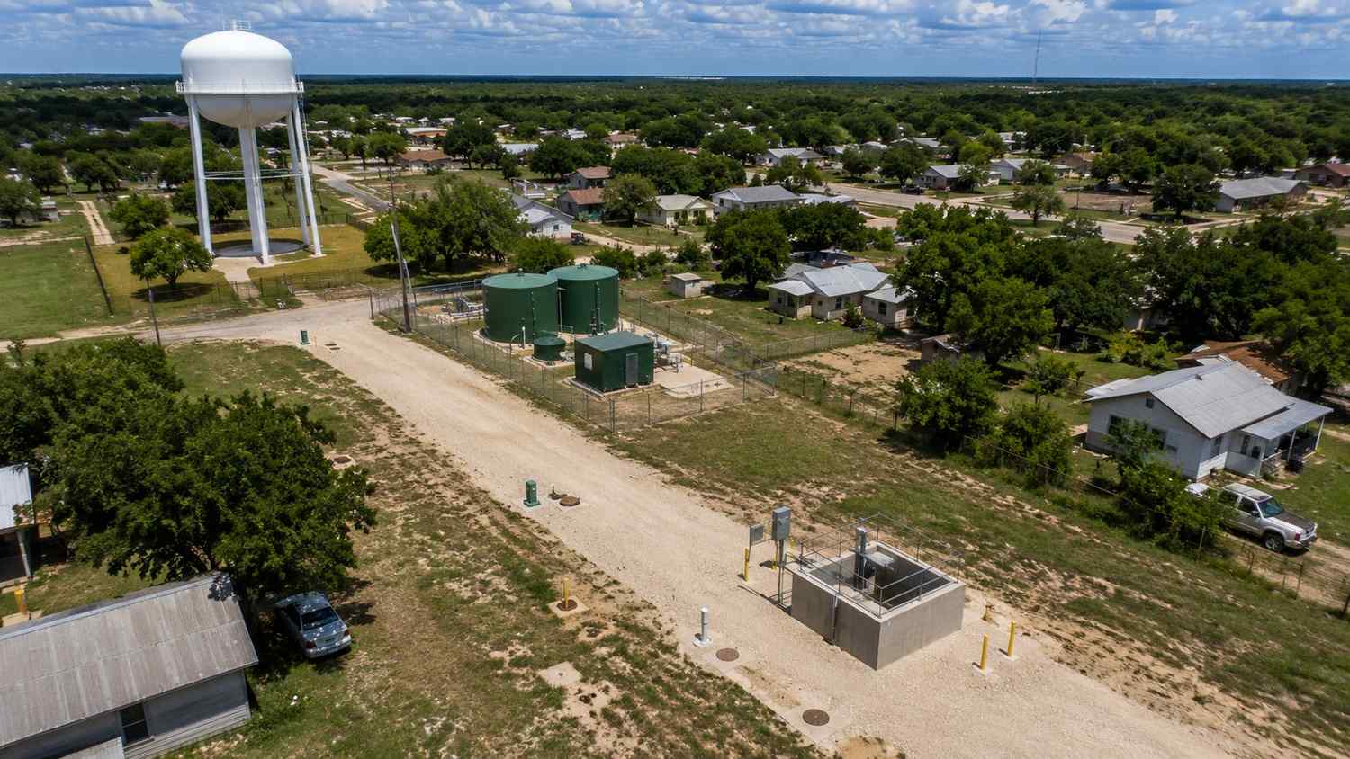 Top-down aerial view of a small Texas municipality showing aging water and wastewater infrastructure including a lift station, water tower, collection mains, and treatment facility representing the assets that belong in a capital improvement plan