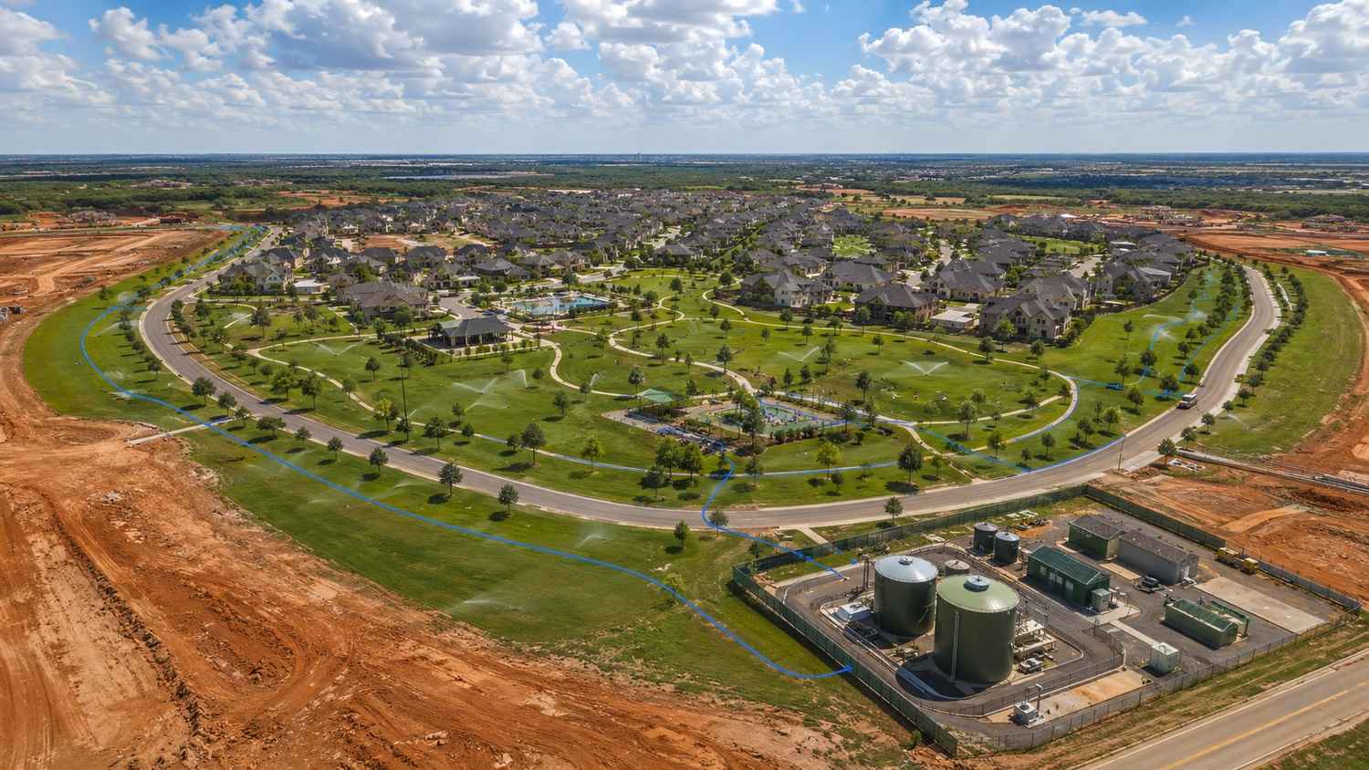 Top-down aerial view of a Texas master-planned development showing reclaimed water irrigation system actively watering green common areas, parks, and landscape buffers with a private wastewater treatment facility visible at the site edge under a Chapter 210 reuse authorization