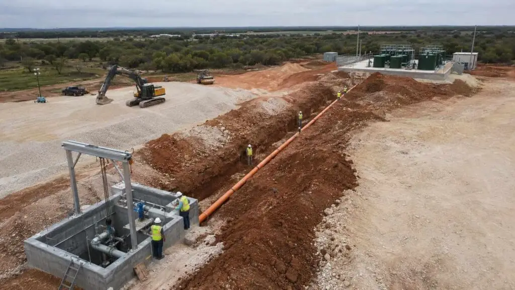 Newly installed Texas lift station wet well with dual submersible pumps, force main pipes, stainless steel hoist frame, and electrical control panel serving a wastewater collection system upstream of a package treatment plant 2