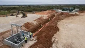 Newly installed Texas lift station wet well with dual submersible pumps, force main pipes, stainless steel hoist frame, and electrical control panel serving a wastewater collection system upstream of a package treatment plant 2