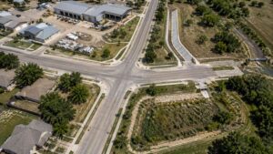 Top-down aerial view of a small Texas city showing storm sewer infrastructure including street drainage inlets, outfall structures discharging to a creek, and municipal facilities representing the regulated MS4 system requiring Phase II permit compliance