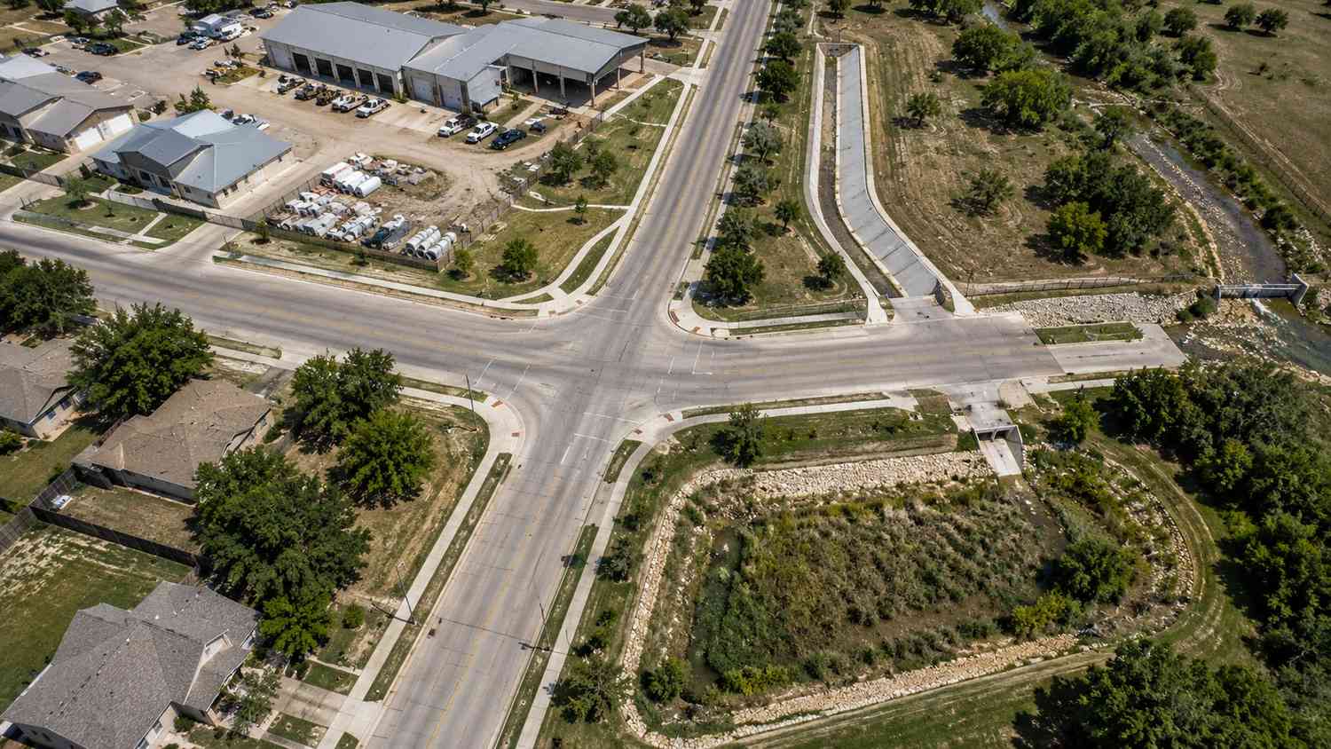Top-down aerial view of a small Texas city showing storm sewer infrastructure including street drainage inlets, outfall structures discharging to a creek, and municipal facilities representing the regulated MS4 system requiring Phase II permit compliance