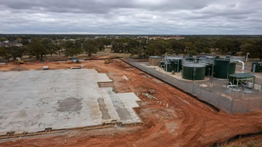 Wastewater engineer and architect reviewing overlapping site plan and wastewater infrastructure layout at a Texas development project showing treatment plant siting, lift station locations, and force main routing coordinated with building footprints