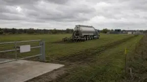 Wide shot of a biosolids land application operation at a Texas agricultural field showing a tanker truck spreading treated sludge across a flat pasture with a private wastewater treatment facility visible at the field edge representing the Chapter 312 compliant disposal pathway that Modern Engineering Solutions helps private WWTP owners establish before plant startup