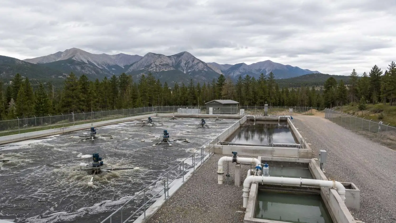 Ground-level shot of a Colorado package wastewater treatment plant showing extended aeration basin with surface aeration equipment and secondary clarifier in a mountain setting evaluated by Modern Engineering Solutions.
