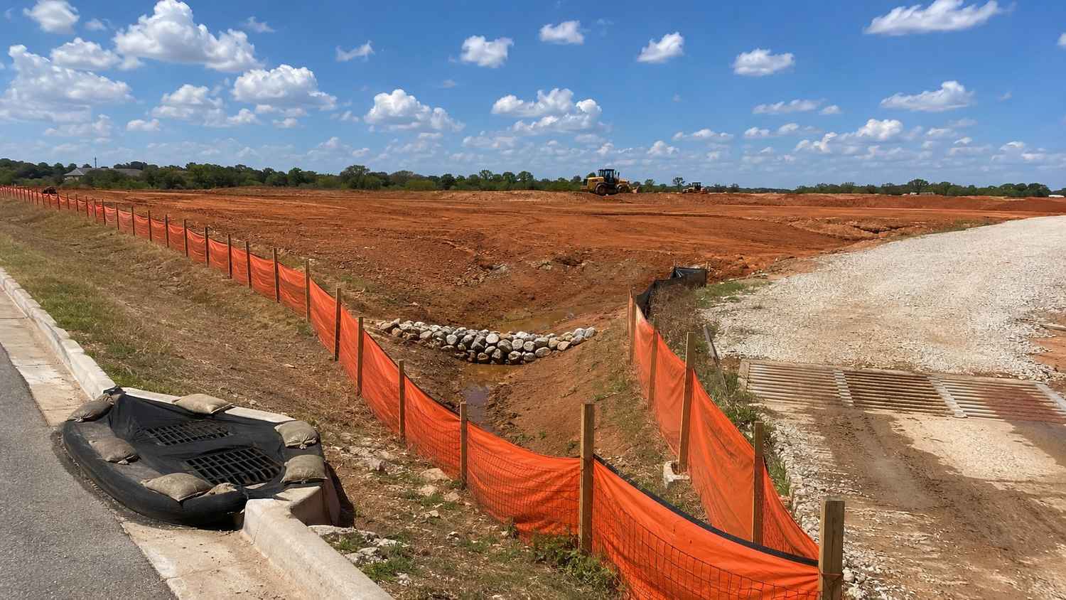 Texas construction site showing properly installed erosion and sediment controls including silt fence along the site perimeter, storm drain inlet protection devices at curb openings, and a stabilized construction entrance preventing sediment tracking onto public roads