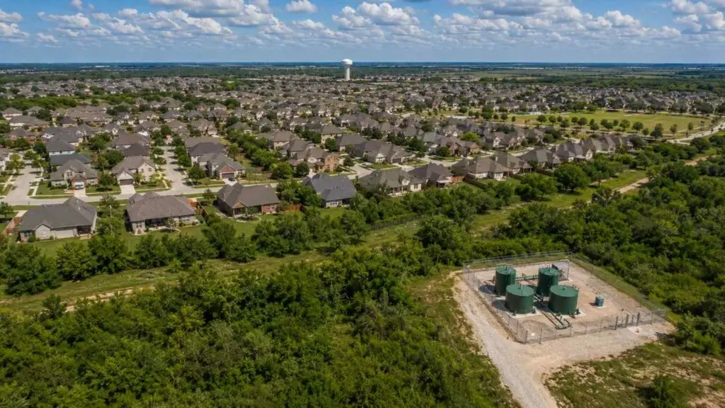 Top-down aerial view of a Texas master-planned residential subdivision showing a private wastewater treatment facility with green cylindrical tanks and chain-link fencing at the development edge with completed homes and streets visible throughout the community representing the privately owned TPDES-permitted treatment systems Modern Engineering Solutions designs and permits for Texas developers