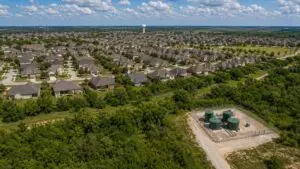 Top-down aerial view of a Texas master-planned residential subdivision showing a private wastewater treatment facility with green cylindrical tanks and chain-link fencing at the development edge with completed homes and streets visible throughout the community representing the privately owned TPDES-permitted treatment systems Modern Engineering Solutions designs and permits for Texas developers