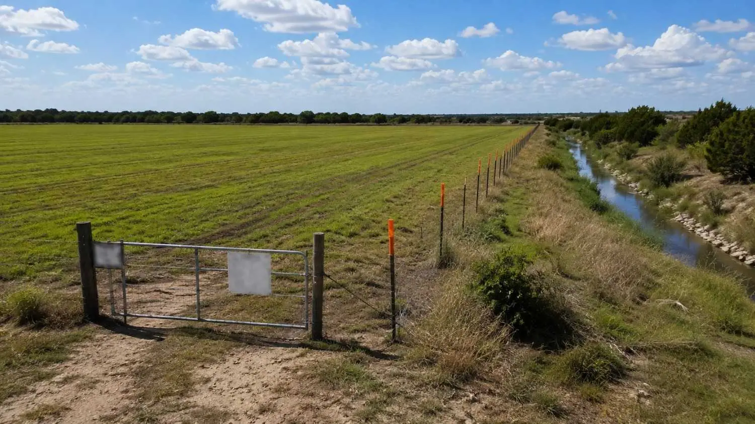 Agricultural land application site boundary in Texas showing setback marker posts at a water feature boundary and fence line representing the site approval and setback documentation requirements for biosolids land application permits under TCEQ Chapter 312