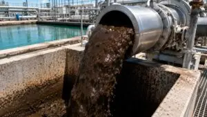 Close-up shot of thick brown digested sewage sludge flowing from a large discharge pipe at a Texas wastewater treatment facility into a holding basin showing the material characteristics of Class B biosolids before land application